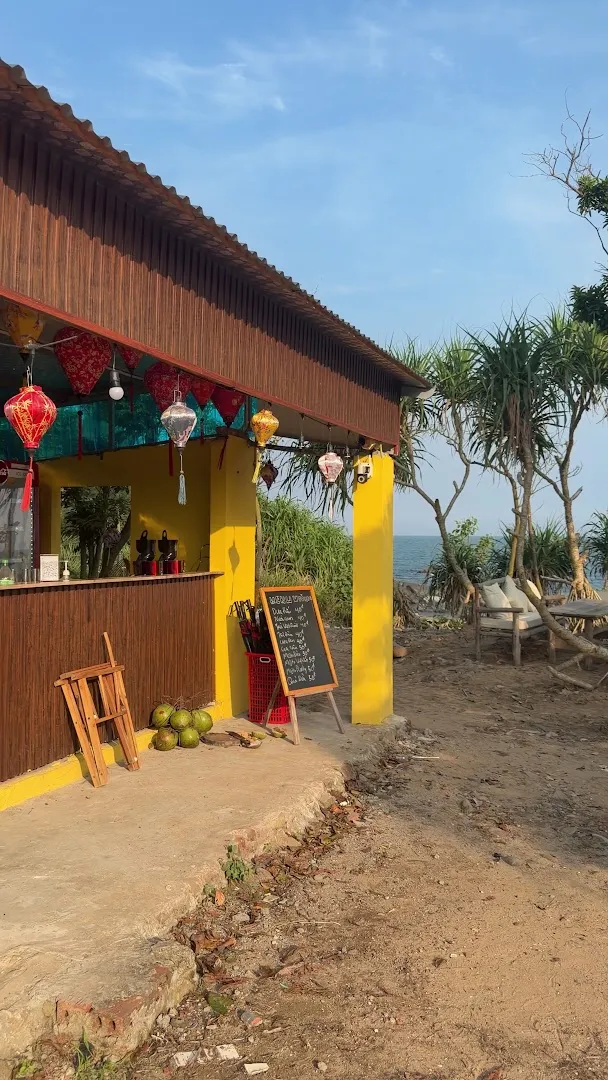 Quầy cà phê ngoài trời với đèn lồng, bảng menu và khung cảnh biển phía sau.