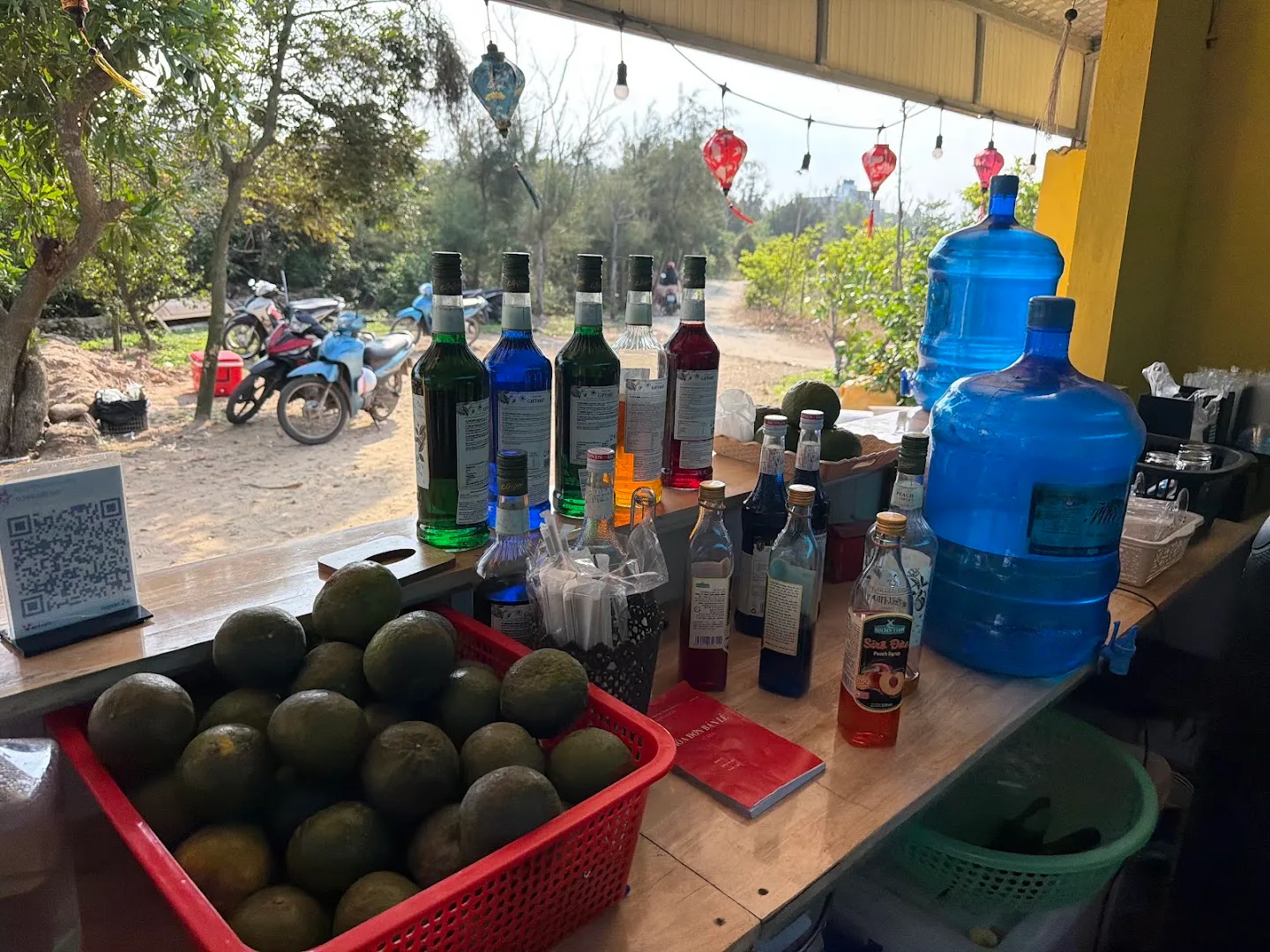 Quầy pha chế với các chai đồ uống, trái cây và bình nước lớn.