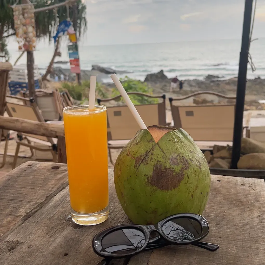 Nước cam và trái dừa tươi trên bàn quán nhìn ra bãi đá và biển.