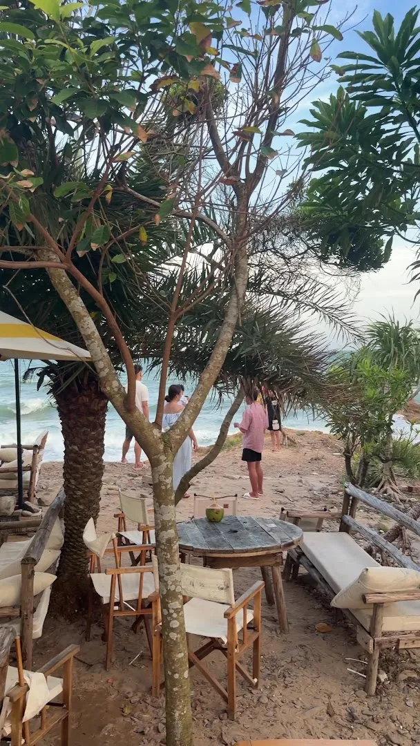 Không gian bàn ghế ngoài trời bên bãi biển, giữa hàng cây nhiệt đới.