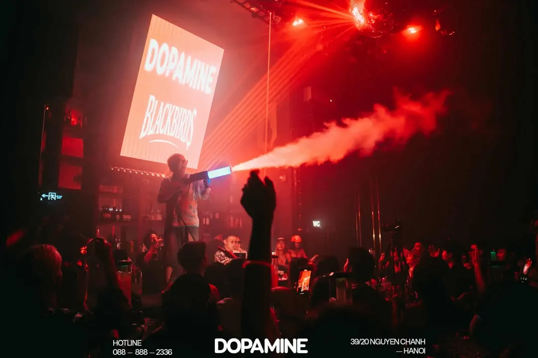 Không gian bar Dopamine với sân khấu, ánh đèn đỏ và màn phun khói giữa đám đông.