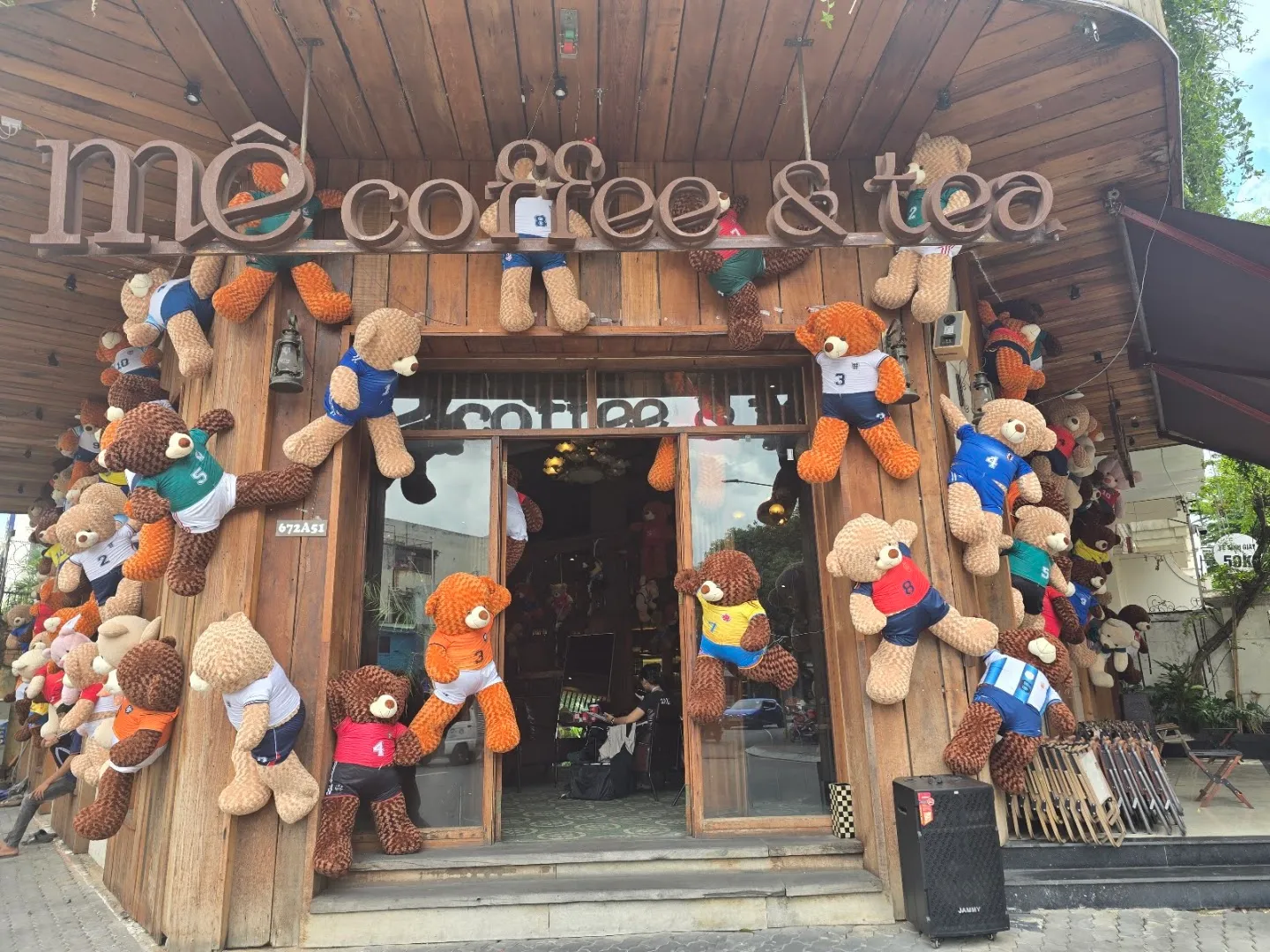 Mặt tiền quán cà phê bằng gỗ với bảng hiệu “me coffee & tea” và nhiều gấu bông trang trí.