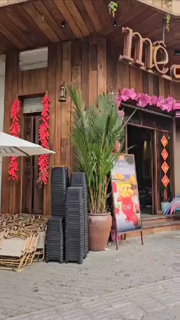 Mặt tiền quán cà phê với cửa gỗ, cây xanh và bảng giới thiệu đồ uống.