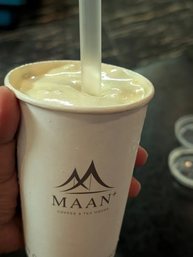 Cốc đồ uống sữa màu kem với logo MAAN Coffee & Tea House.