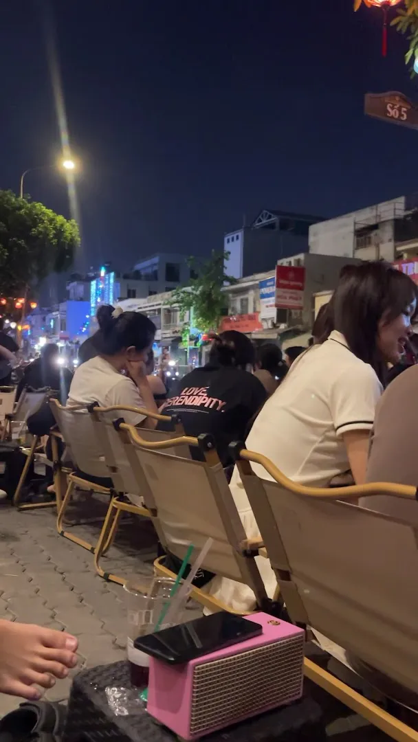 Không gian ngồi ngoài trời buổi tối với nhiều khách và ghế xếp bên vỉa hè.