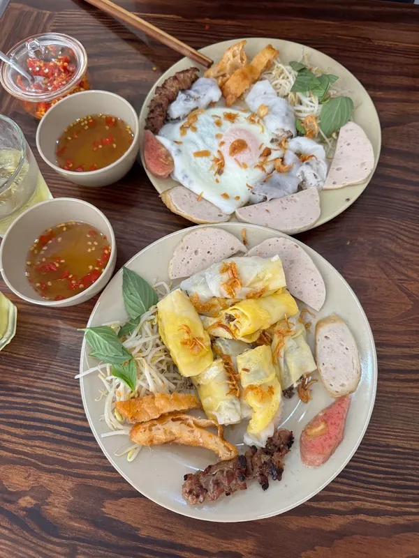 Hai đĩa món ăn Việt với bún, chả giò, thịt nướng, chả lụa, rau sống và nước chấm.