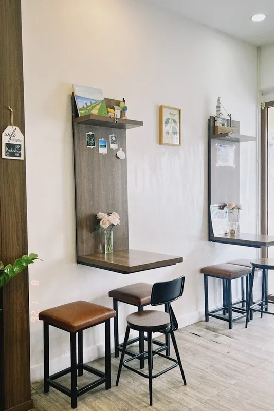 Không gian quán cà phê sáng sủa với ghế bar và kệ trang trí tối giản.