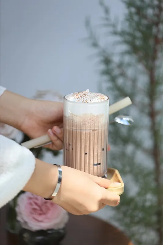 Ly cà phê sữa phủ bọt kem trên khay gỗ.