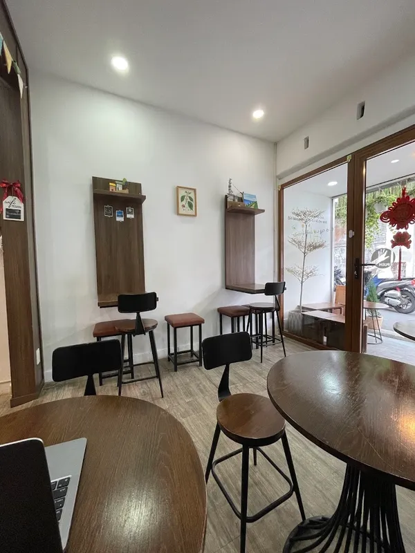 Không gian bên trong quán với bàn ghế gỗ và cửa kính nhìn ra bên ngoài.