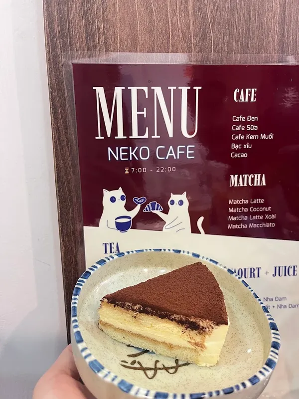 Bánh tiramisu đặt trước bảng menu Neko Cafe.