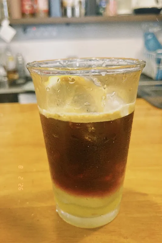 Ly cà phê đá với lớp bọt và lát chanh trong ly nhựa.