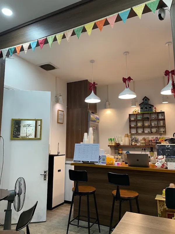 Không gian quầy bar và khu vực ngồi bên trong quán cà phê, với đèn treo và kệ trang trí.