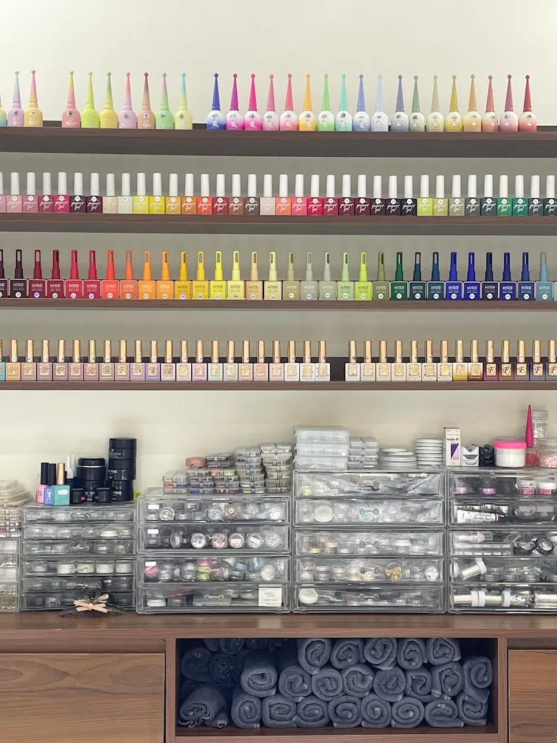Kệ trưng bày nhiều màu sơn móng, phụ kiện làm nail và khăn cuộn.