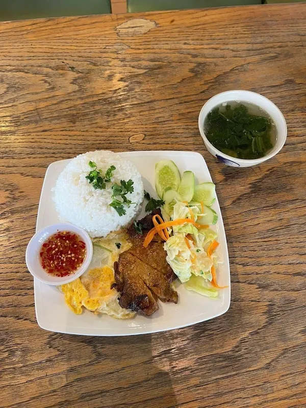 Suất cơm với thịt nướng, trứng chiên, rau củ, nước chấm và canh.
