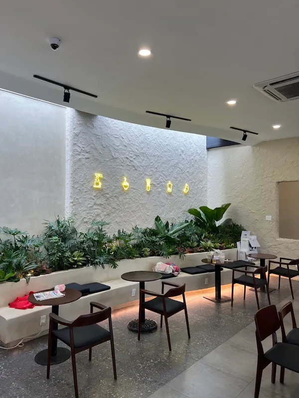 Không gian quán với bàn ghế, cây xanh và tường đèn neon trang trí.