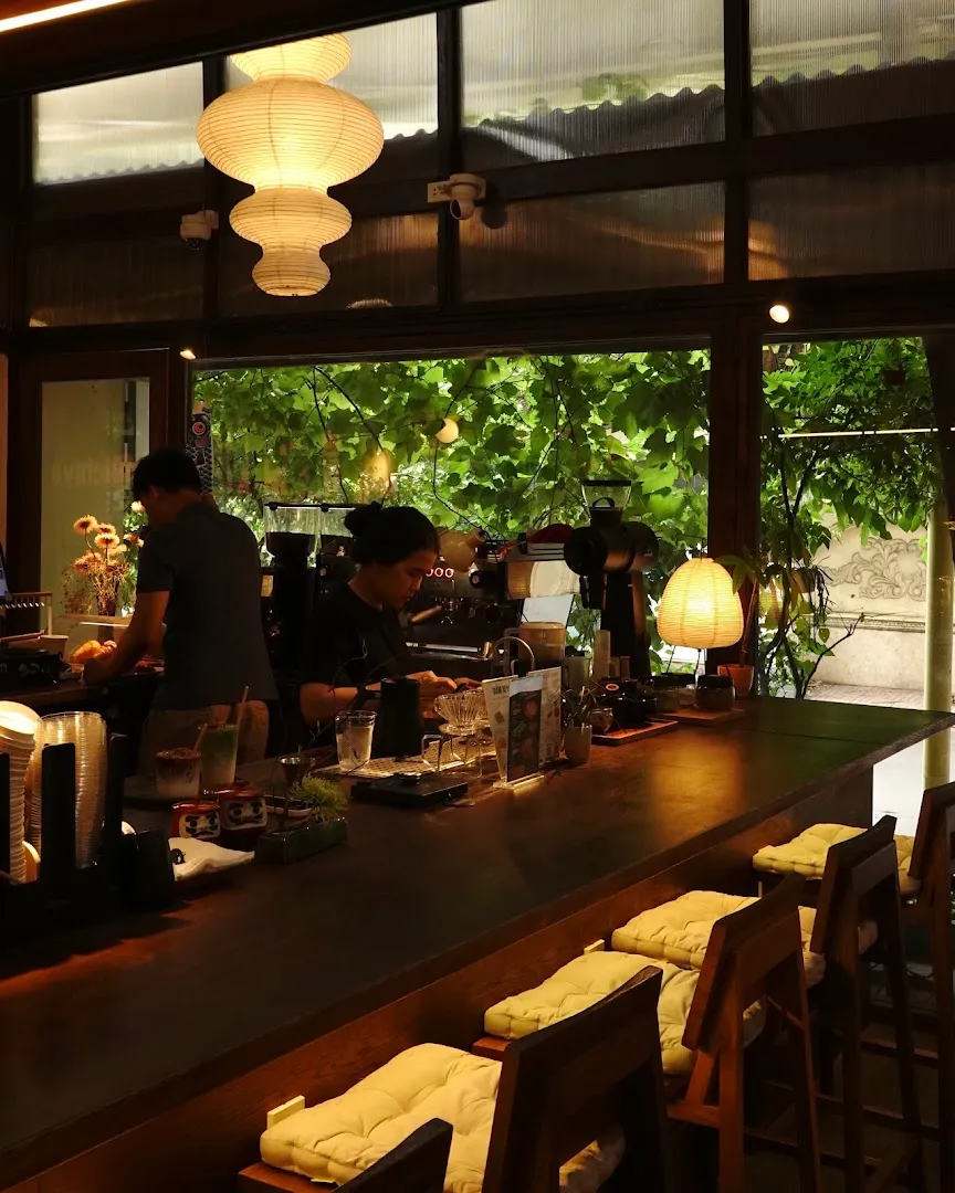 Không gian quầy bar ấm cúng với đèn lồng, máy pha cà phê và chỗ ngồi nhìn ra mảng xanh.