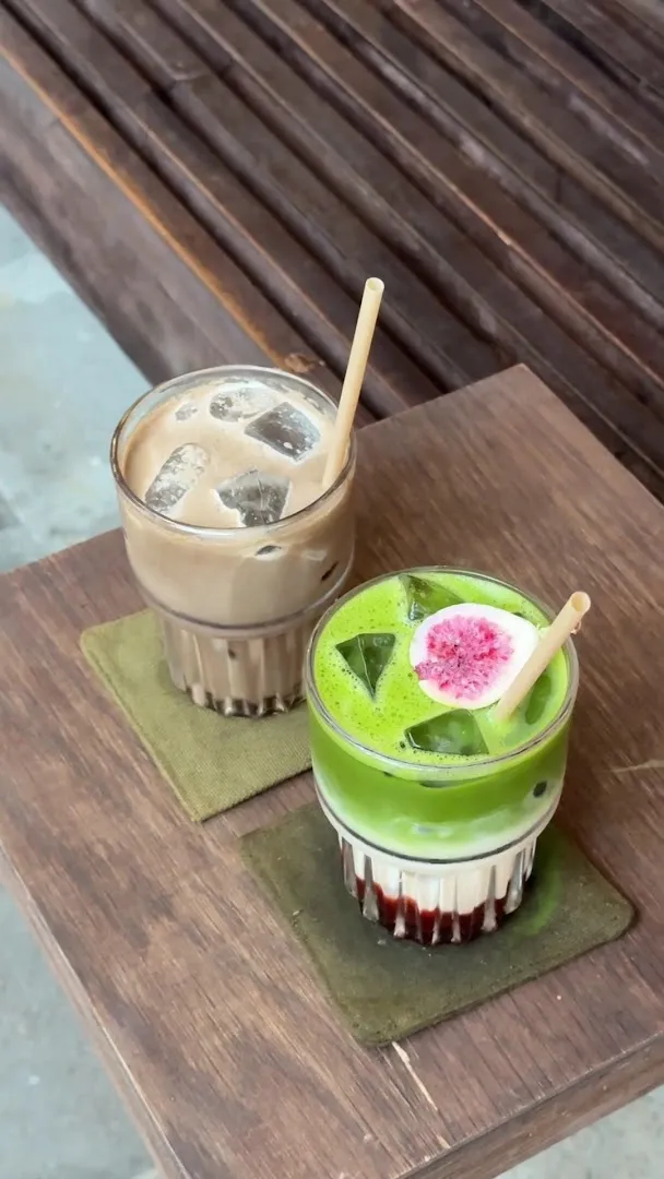 Hai ly đồ uống đá, gồm một ly cà phê sữa và một ly trà xanh trang trí hoa.