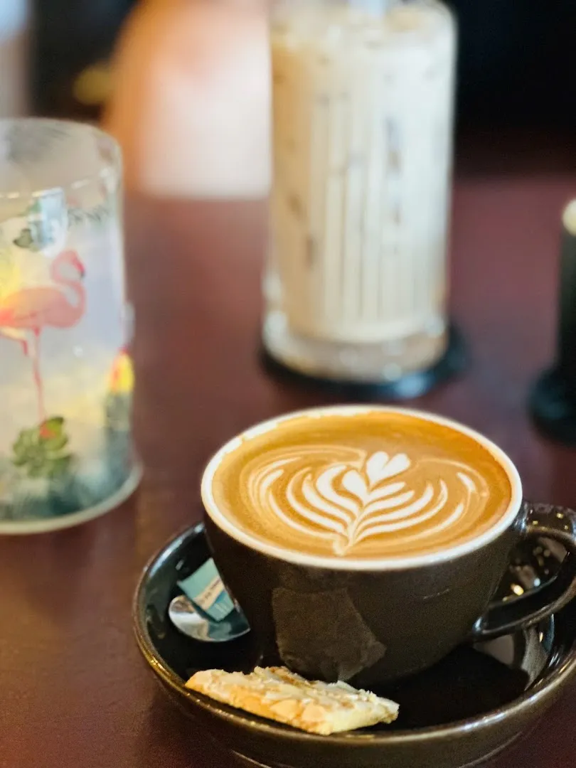 Tách cà phê latte với họa tiết bọt sữa, kèm bánh quy trên đĩa.