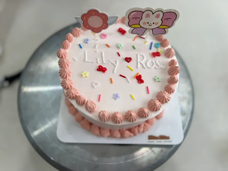 Bánh kem trang trí chữ “Lily Rose”, viền kem hồng và cốm màu sắc.
