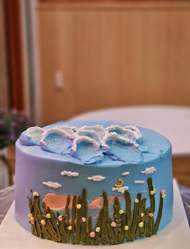 Bánh kem xanh trang trí họa tiết cỏ và hoa nhỏ.