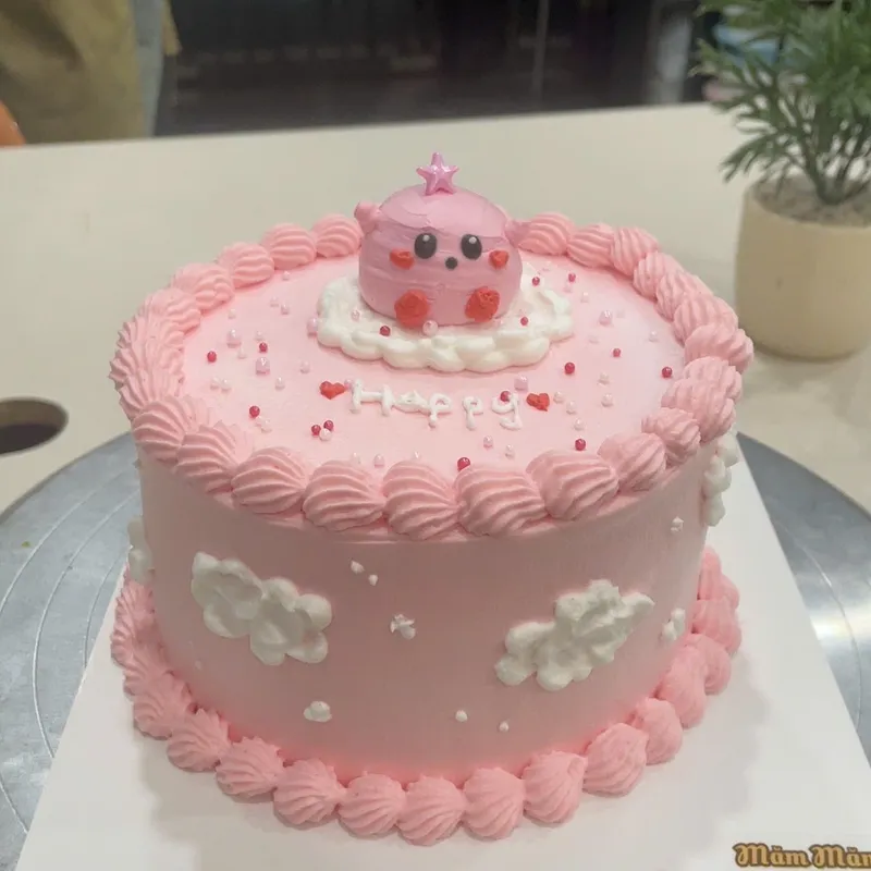 Bánh kem màu hồng trang trí nhân vật đáng yêu, ngôi sao và dòng chữ “Happy”.