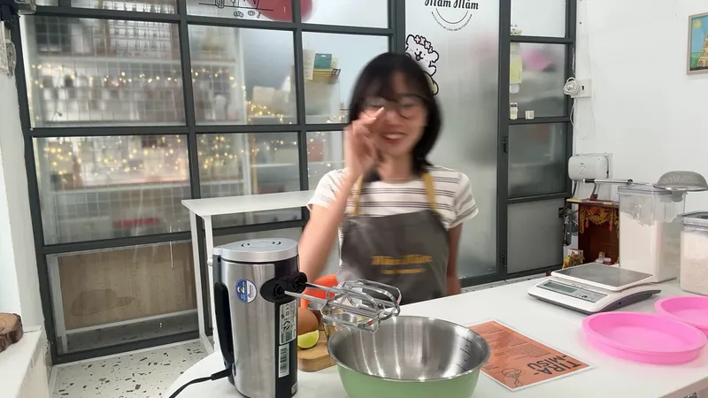 Không gian làm bánh với dụng cụ trộn và cân điện tử trên bàn, cùng một người mặc tạp dề.