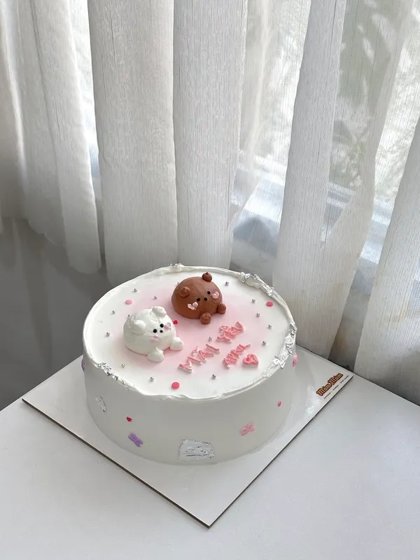 Bánh kem trang trí hình thú với lời chúc màu hồng và họa tiết dễ thương.